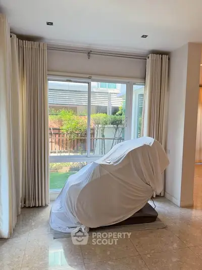 Spacious living room with large windows and garden view, featuring elegant curtains and marble flooring.