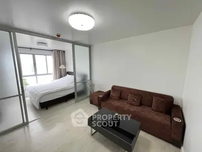 Modern living room with brown sofa and glass partition leading to a bright bedroom.