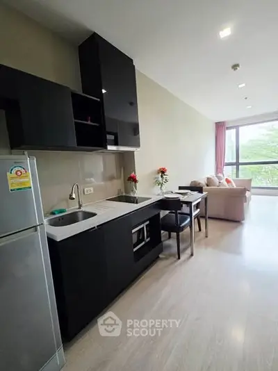 Modern open-layout kitchen with sleek black cabinets and cozy living area with large window view.