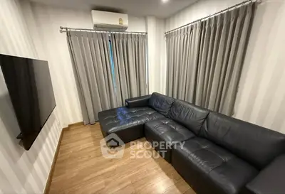 Modern living room with sleek black leather sofa and wall-mounted TV, featuring elegant curtains and wooden flooring.