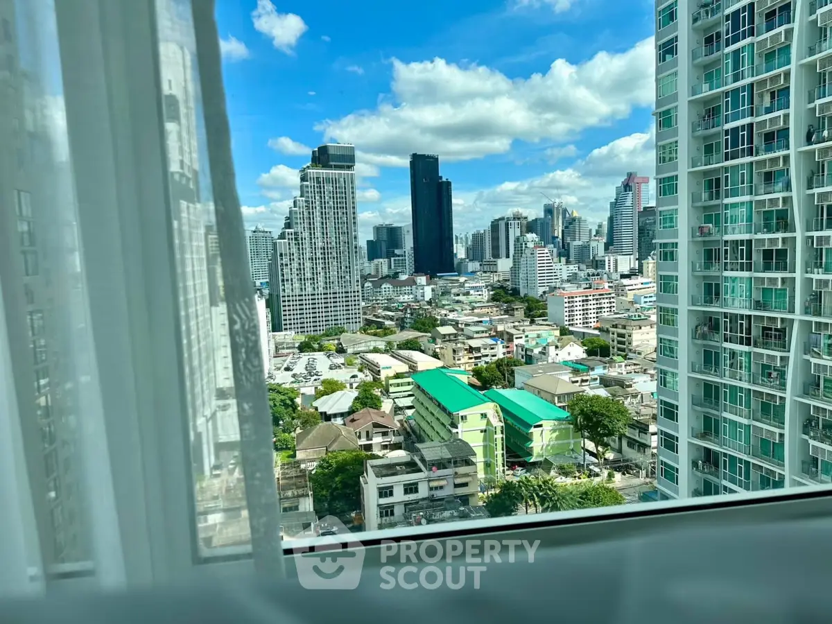 Stunning cityscape view from a high-rise apartment window with modern buildings and blue sky.