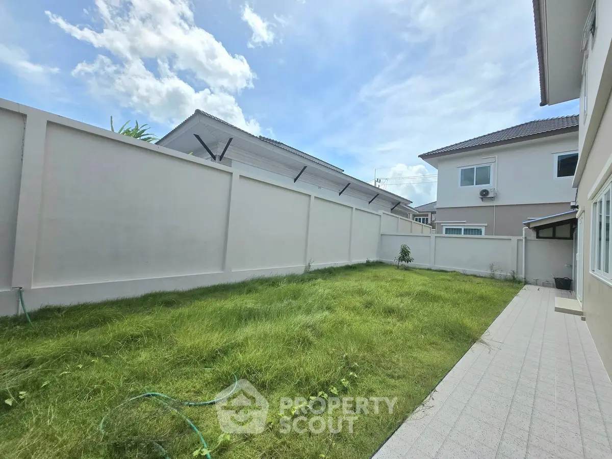 Spacious backyard with lush green lawn and modern house exterior under a clear blue sky.