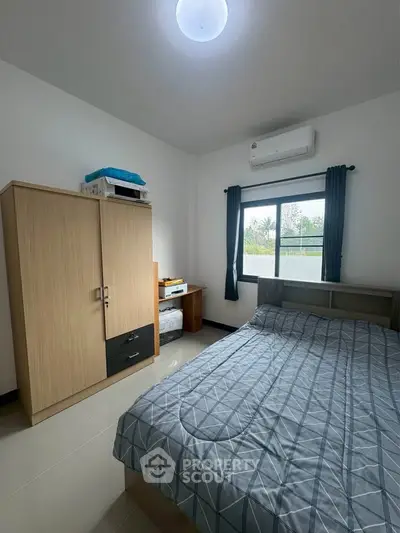 Cozy bedroom with modern furnishings and natural light, featuring a wardrobe and air conditioning.