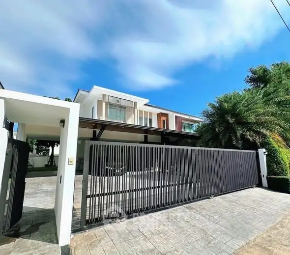 Modern luxury home with sleek gate and lush greenery under a clear blue sky.