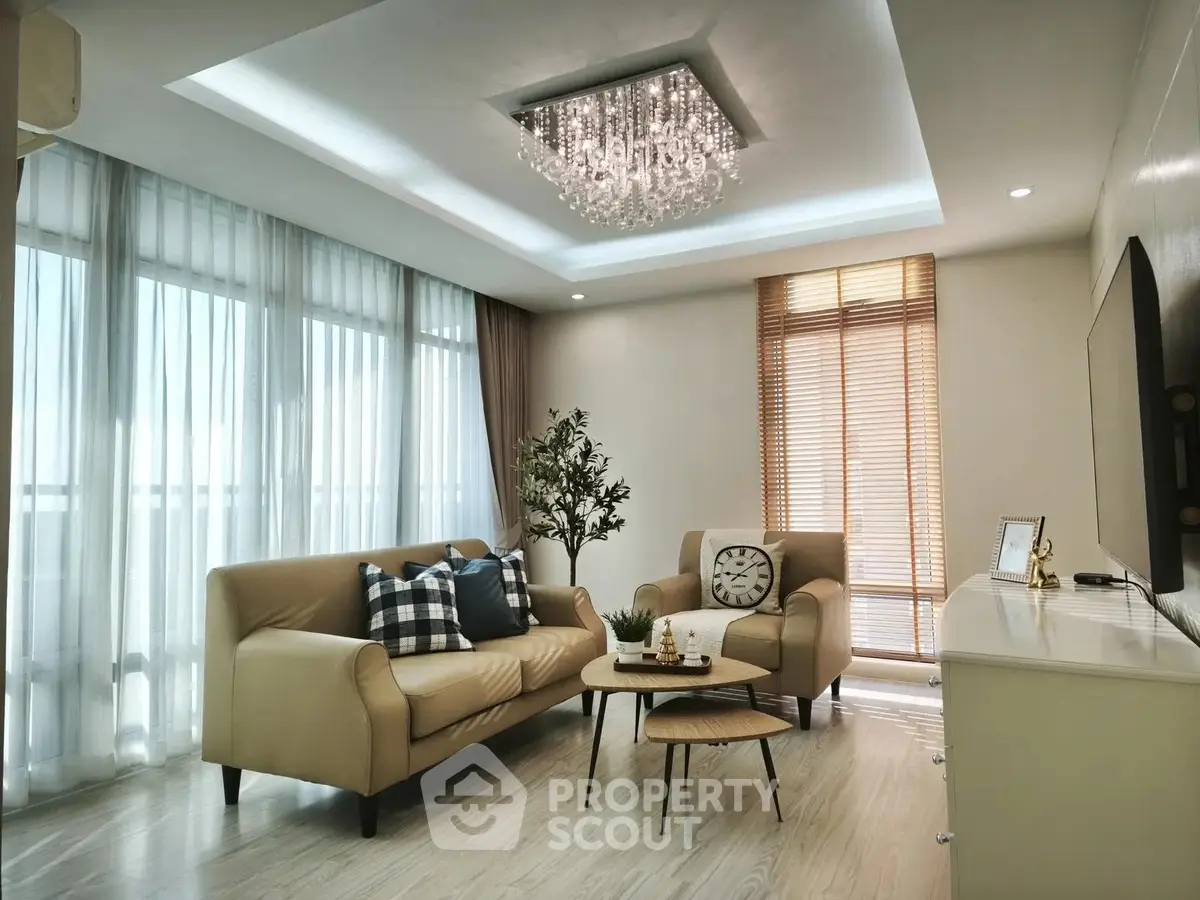 Elegant living room with modern chandelier and cozy seating area, featuring floor-to-ceiling windows and stylish decor.