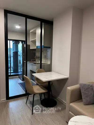 Modern apartment interior with compact dining area and glass partition to kitchen.