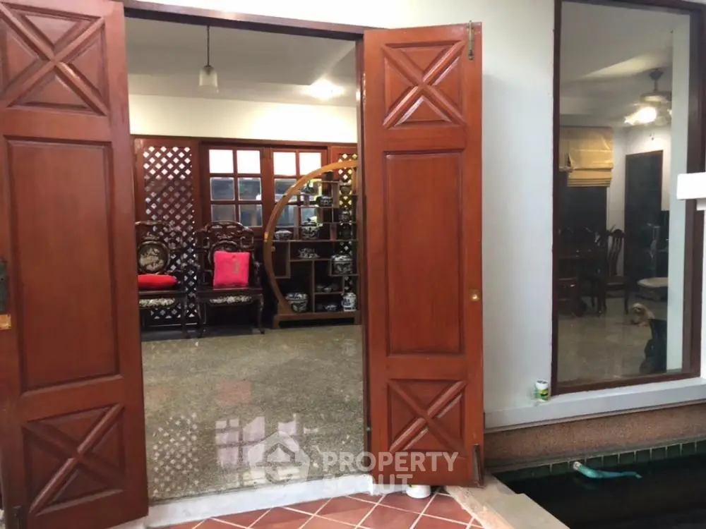 Elegant home entrance with open wooden doors leading to a spacious living area with traditional furniture and decorative partitions.
