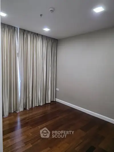 Spacious empty room with wooden flooring and elegant curtains