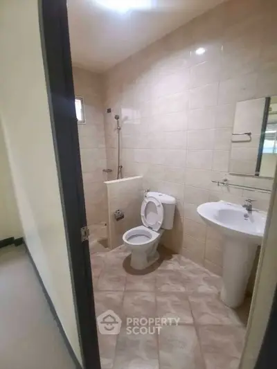 Modern bathroom with tiled walls and floor, featuring a toilet and pedestal sink.