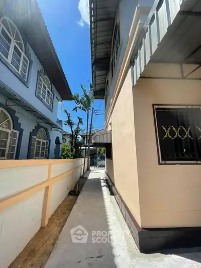 Narrow pathway between two residential buildings under a clear blue sky.