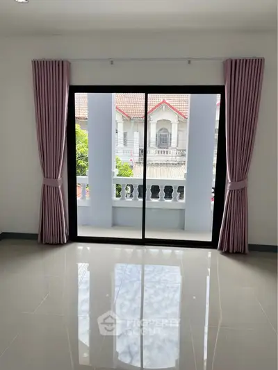 Bright room with large sliding glass doors leading to a balcony, offering a view of neighboring houses.