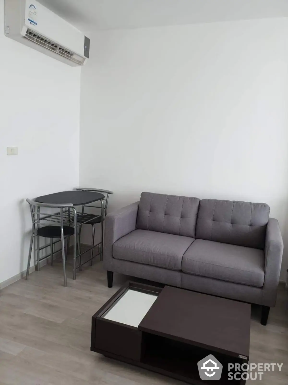 Modern living room with gray sofa, air conditioning, and dining table set.