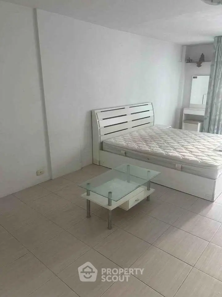 Spacious bedroom with modern white bed and glass table, perfect for minimalist living.