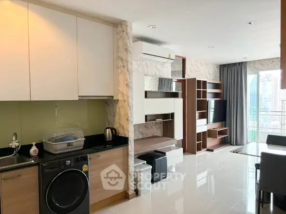 Modern open-plan living room with kitchen featuring sleek appliances and city view balcony.