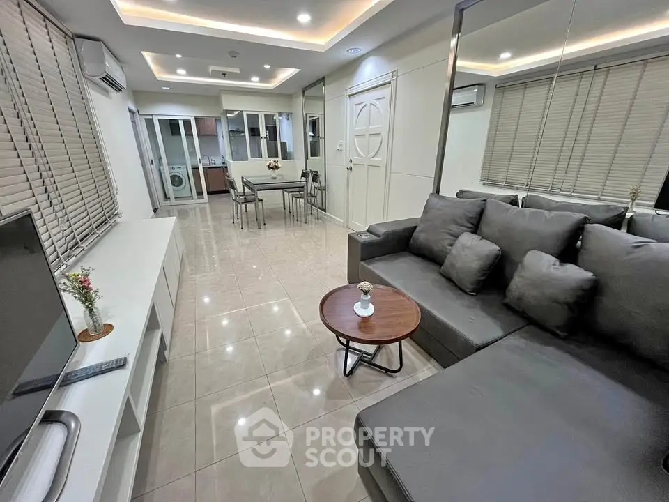 Modern living room with sleek gray sofa and open layout, featuring a dining area and washing machine in view.