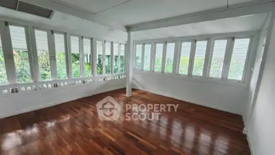 Spacious sunlit room with wooden floors and large windows, perfect for a serene living space.