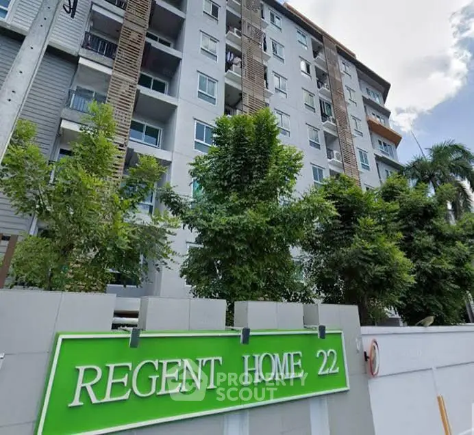 Modern apartment building exterior with lush greenery and clear blue sky.