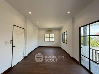 Spacious empty room with wooden flooring and large windows offering natural light and balcony access.
