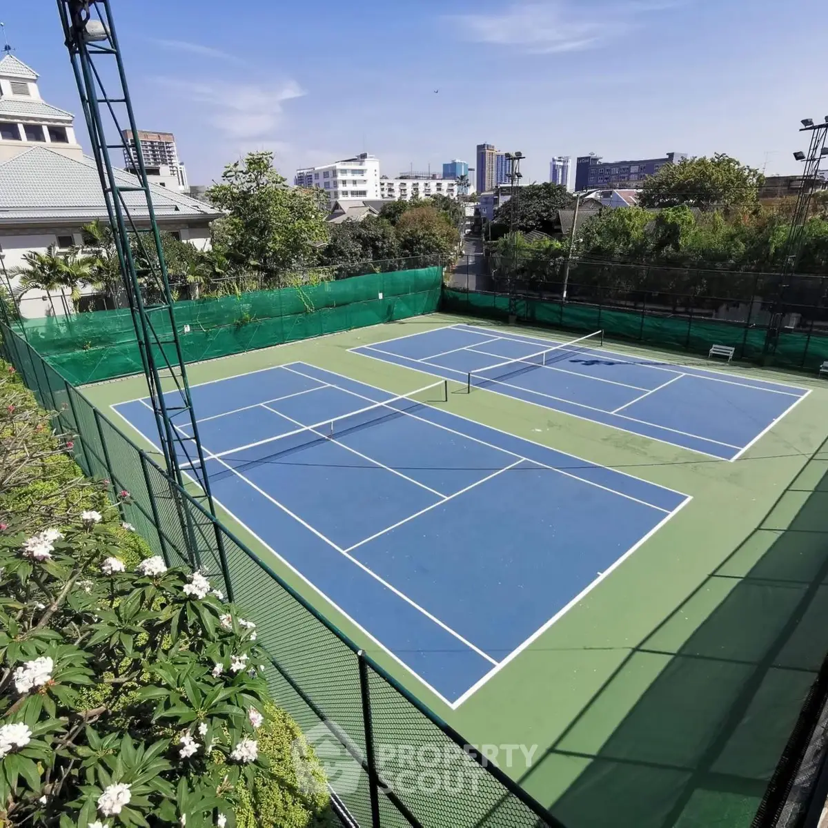 Spacious outdoor tennis court in urban residential complex with lush greenery.