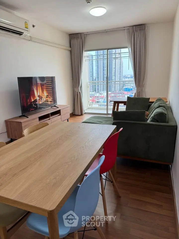 Modern living room with large TV, stylish furniture, and city view balcony in high-rise apartment.
