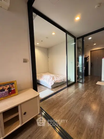 Modern apartment interior with glass-walled bedroom and wooden flooring, showcasing sleek design and cozy ambiance.