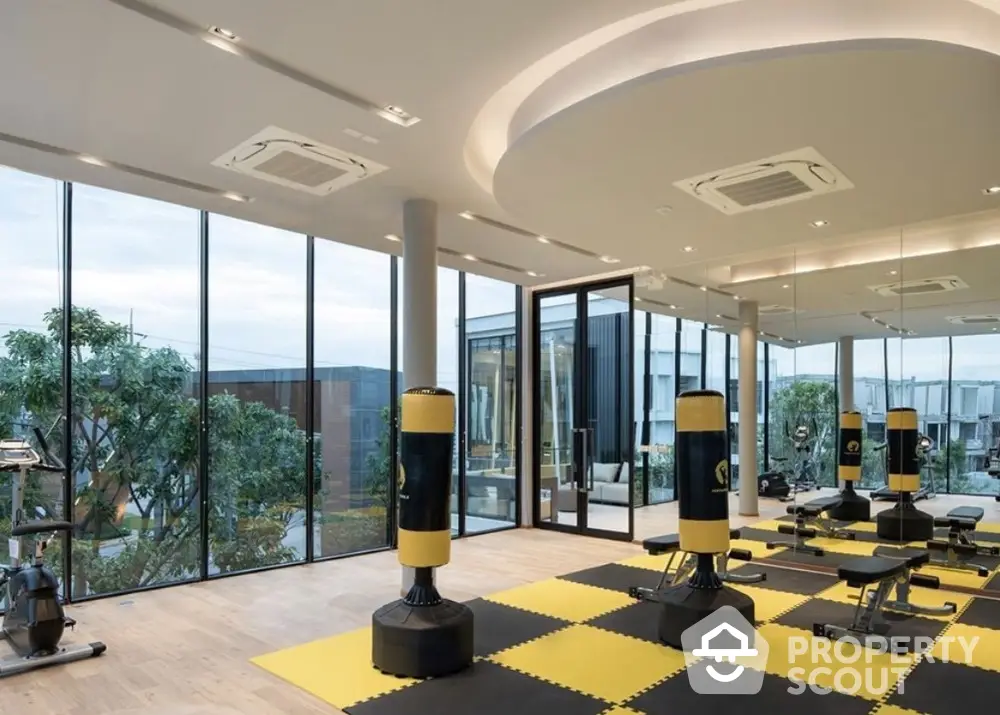 Modern gym with large windows and boxing equipment in luxury building.