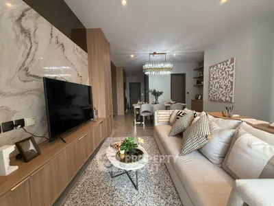 Modern living room with stylish decor and open layout, featuring a large TV and elegant chandelier.