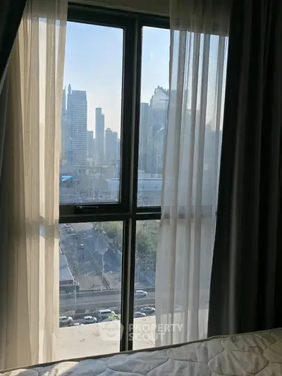 Stunning cityscape view from a cozy bedroom window with sheer curtains, perfect urban living.