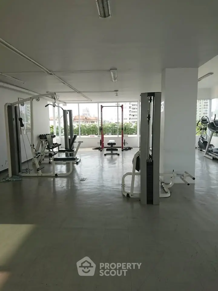 Spacious gym with modern equipment and city view, ideal for fitness enthusiasts.