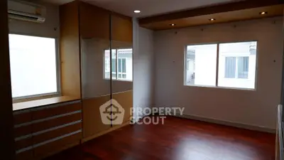 Spacious room with wooden flooring and built-in wardrobe, featuring large windows for natural light.