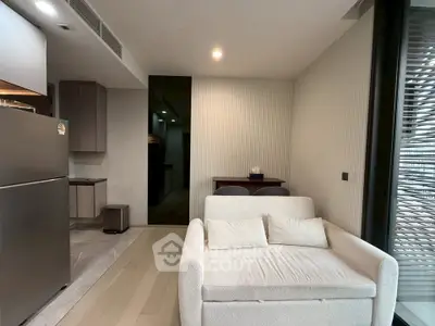 Modern living room with sleek design and open kitchen layout, featuring a cozy sofa and stainless steel appliances.