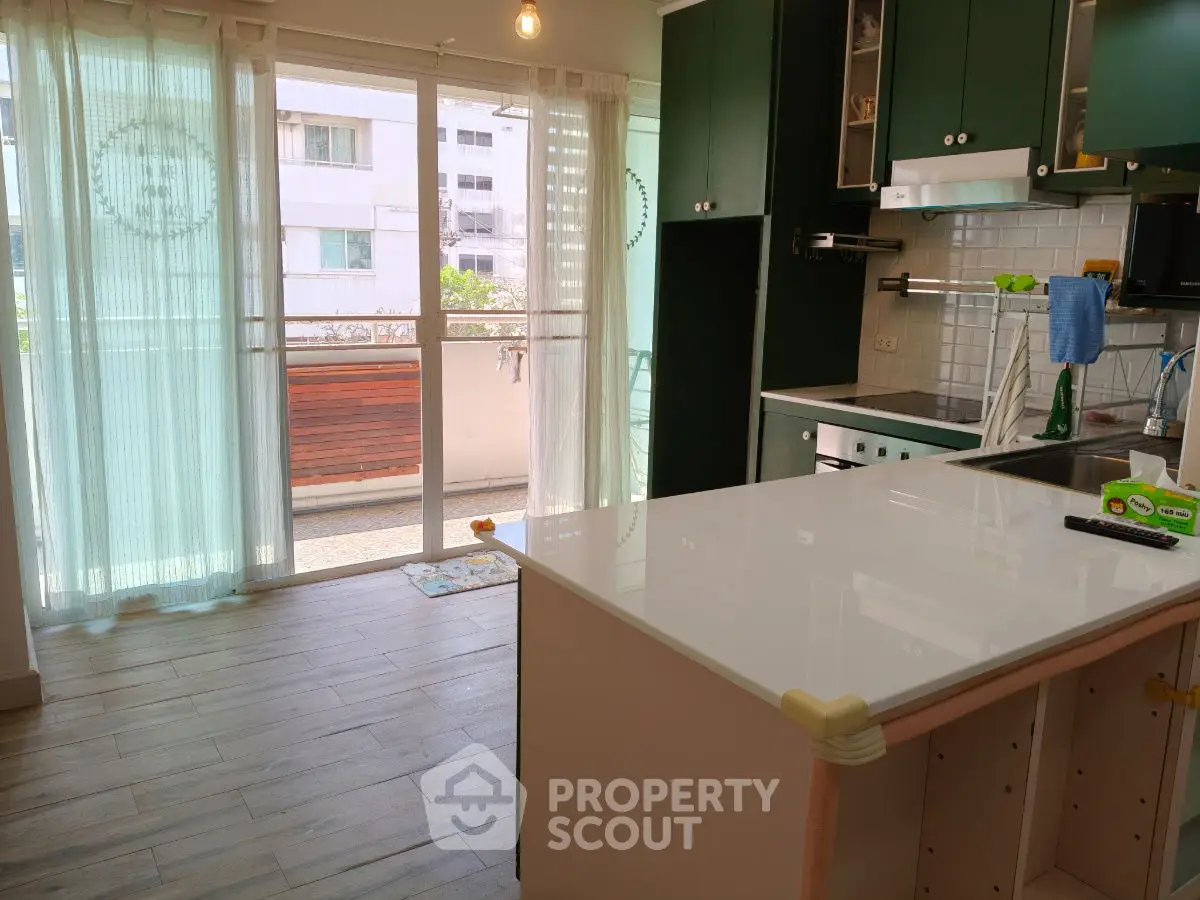 Modern kitchen with green cabinets and balcony view, featuring sleek countertops and ample natural light.