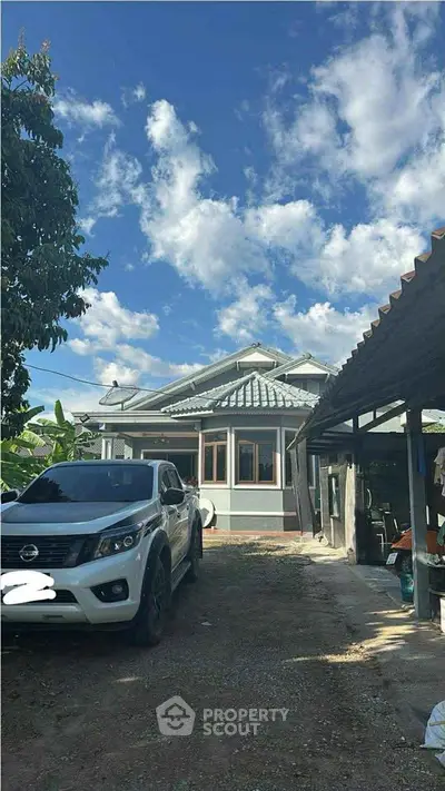 Charming single-story house with a spacious driveway and lush greenery under a clear blue sky.