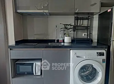 Modern kitchen with washing machine, microwave, and sleek cabinetry in compact layout.