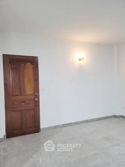 Spacious empty room with wooden door and modern light fixture, perfect for customization.