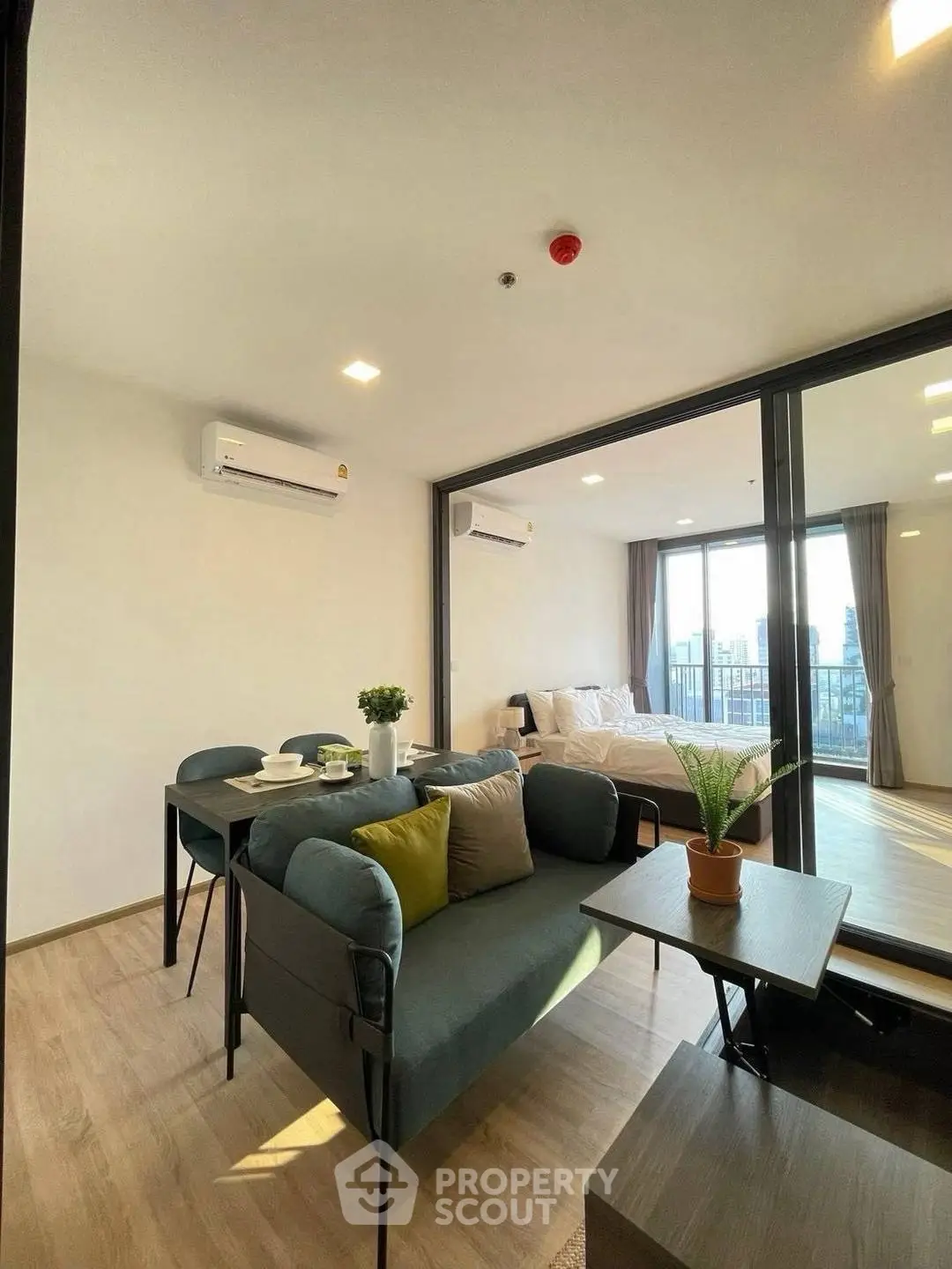 Modern open-plan living room with dining area and bedroom, featuring stylish furniture and large windows.