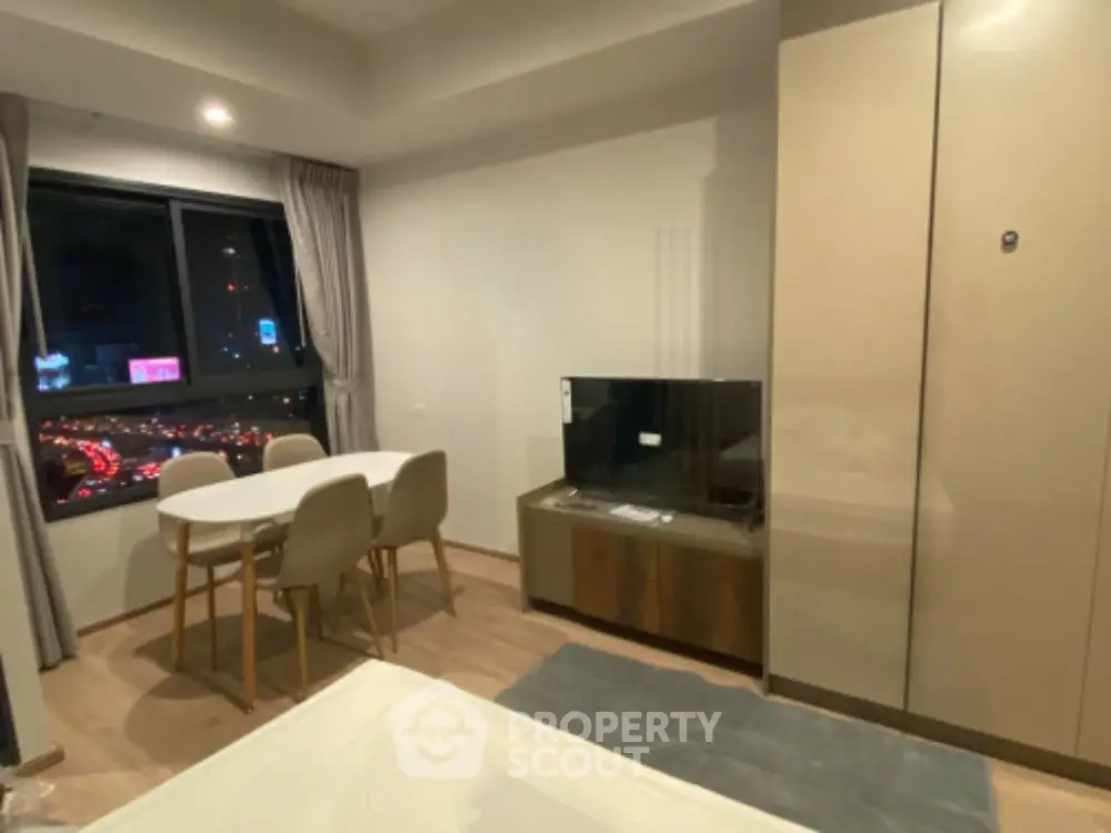 Modern apartment interior with city view, featuring dining area and TV setup.