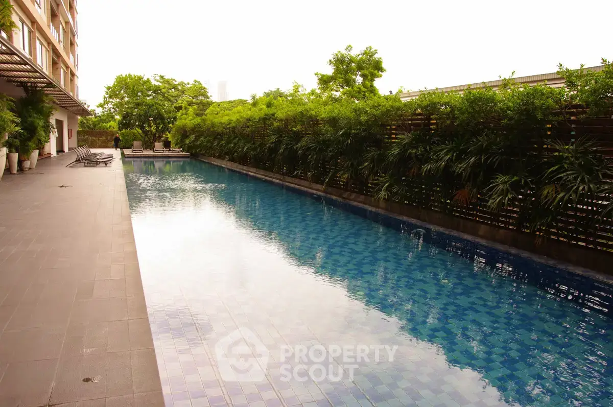Luxurious outdoor swimming pool with lush greenery in modern residential complex.