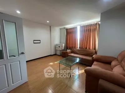Cozy living room with brown leather sofas and glass coffee table, featuring warm natural light.