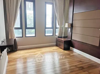 Spacious bedroom with wooden flooring and large windows offering natural light.