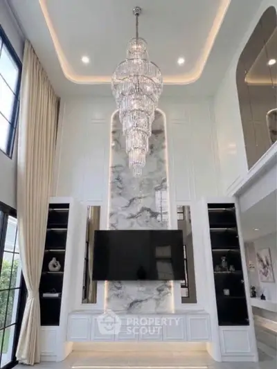 Luxurious living room with high ceiling, elegant chandelier, and modern entertainment center.