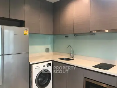 Modern kitchen with sleek cabinets, washing machine, and stainless steel appliances.