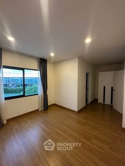 Spacious empty room with wooden flooring and large window offering scenic views.