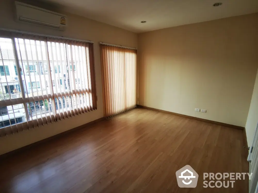 Spacious living room with large windows allowing ample natural light, featuring elegant wooden flooring and a serene view, perfect for family gatherings.