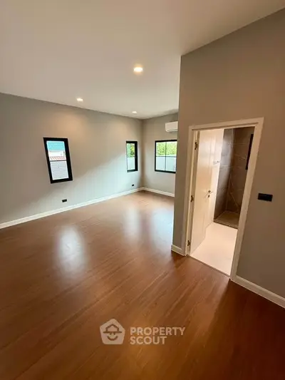 Spacious empty room with wooden flooring and natural light, ideal for customization.