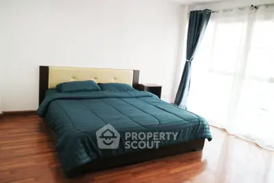 Spacious bedroom with wooden flooring and large window for natural light.