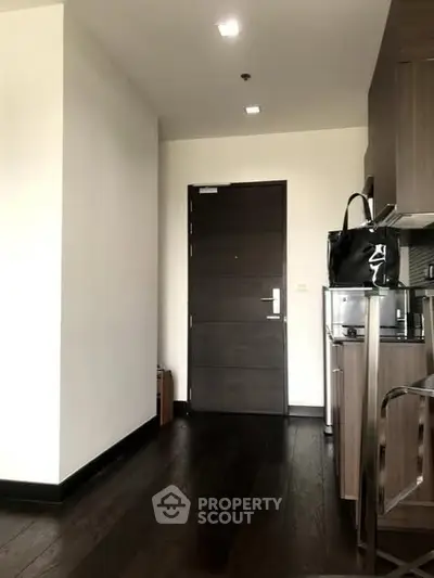 Modern apartment entrance with sleek wooden flooring and stylish kitchen area.