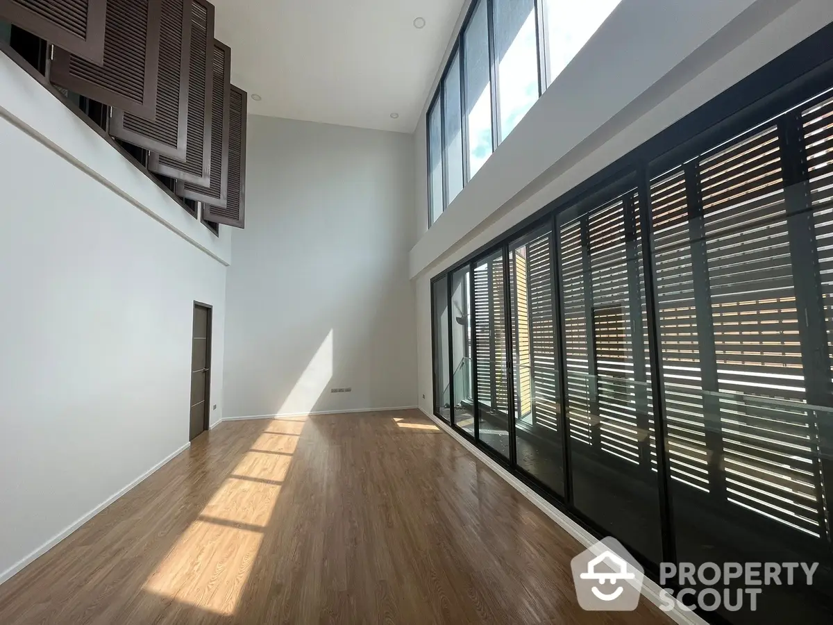 Spacious living room with high ceilings, large windows, and modern wooden flooring, offering a blend of natural light and contemporary design.