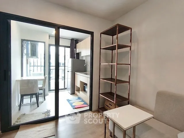 Modern living room with open kitchen and balcony access, featuring sleek shelving and cozy seating.