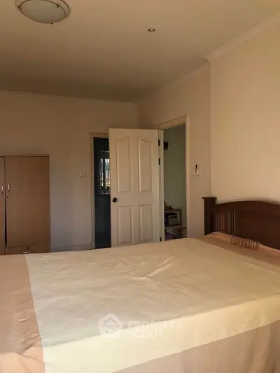 Cozy bedroom with wooden bed frame and wardrobe, featuring neutral tones and natural light.